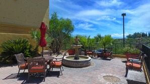 An outdoor patio with wicker furniture, a red umbrella, a fountain, and potted plants. - Hampton Inn & Suites Tucson-Mall (Tucson)