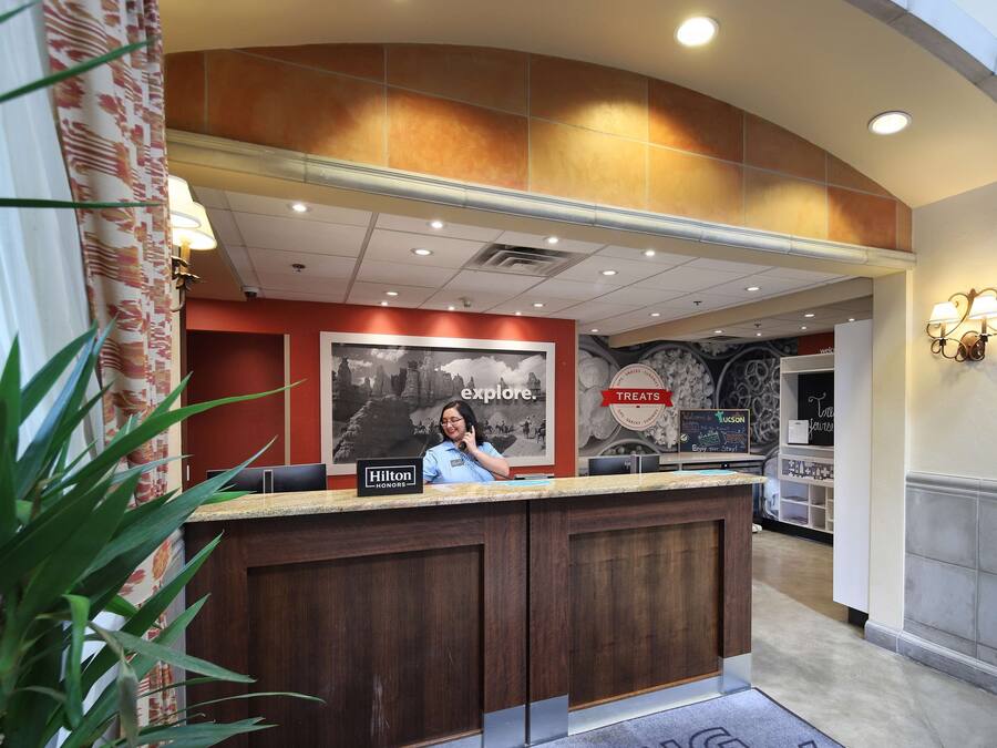A hotel reception desk with a large poster advertising exploration and treats, a receptionist, and a modern interior design.