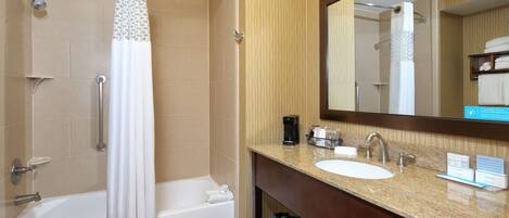 A bathroom with a bathtub, shower, and vanity with a sink and mirror.
