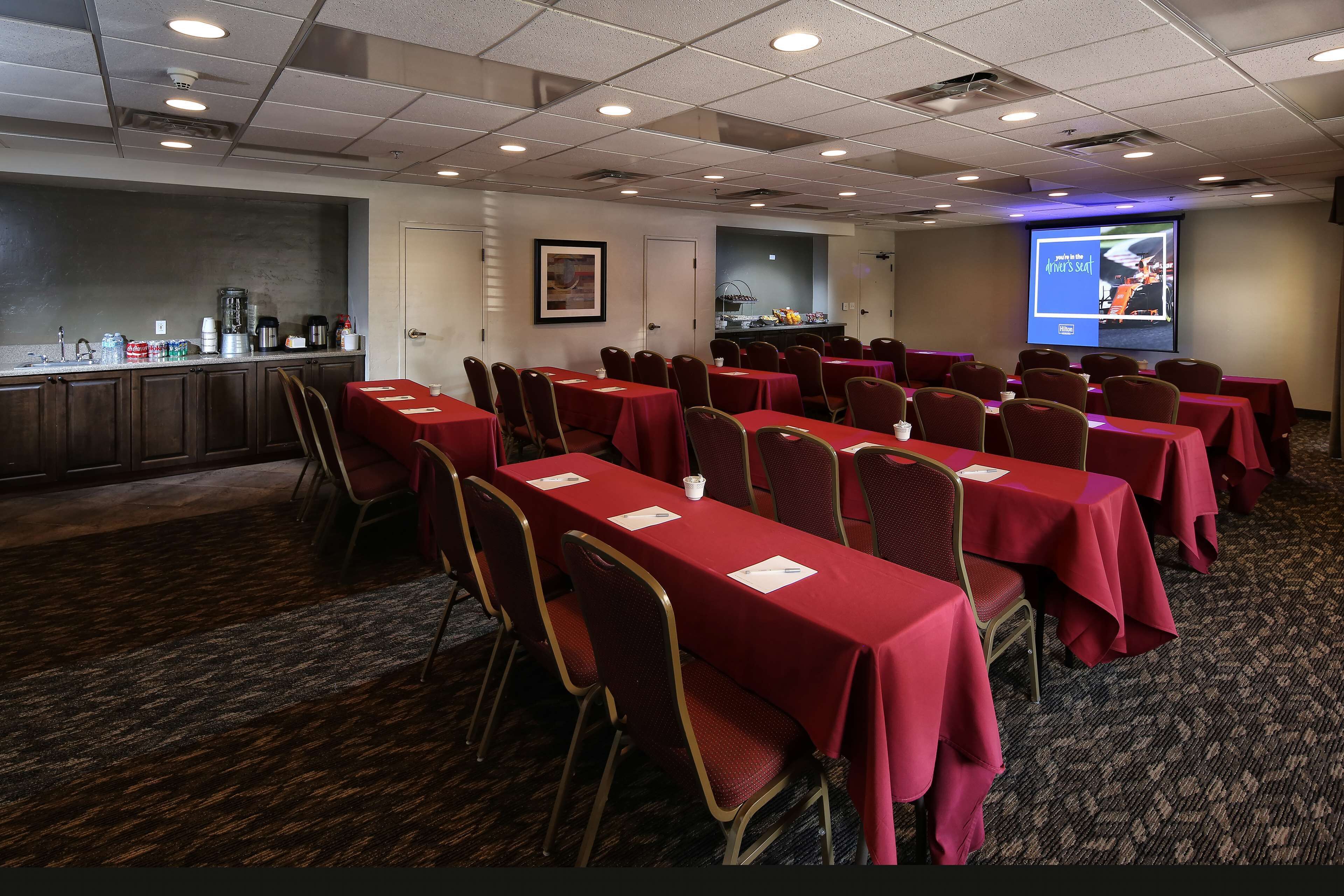A conference room with rows of tables and chairs, a projection screen, and a buffet area.