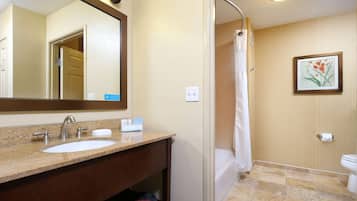 A bathroom with a sink, mirror, shower, toilet, and a framed picture on the wall.