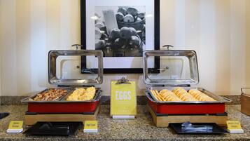 A breakfast buffet with labeled trays of eggs, redskin potatoes, and bagel toppings.