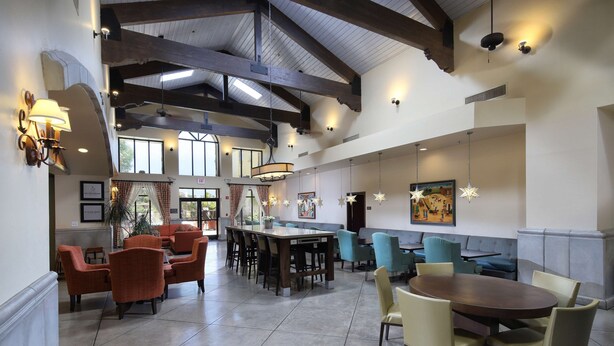 A spacious lobby with high ceilings, exposed beams, and a mix of seating areas including a long communal table and individual chairs. - Hampton Inn & Suites Tucson-Mall (Tucson)