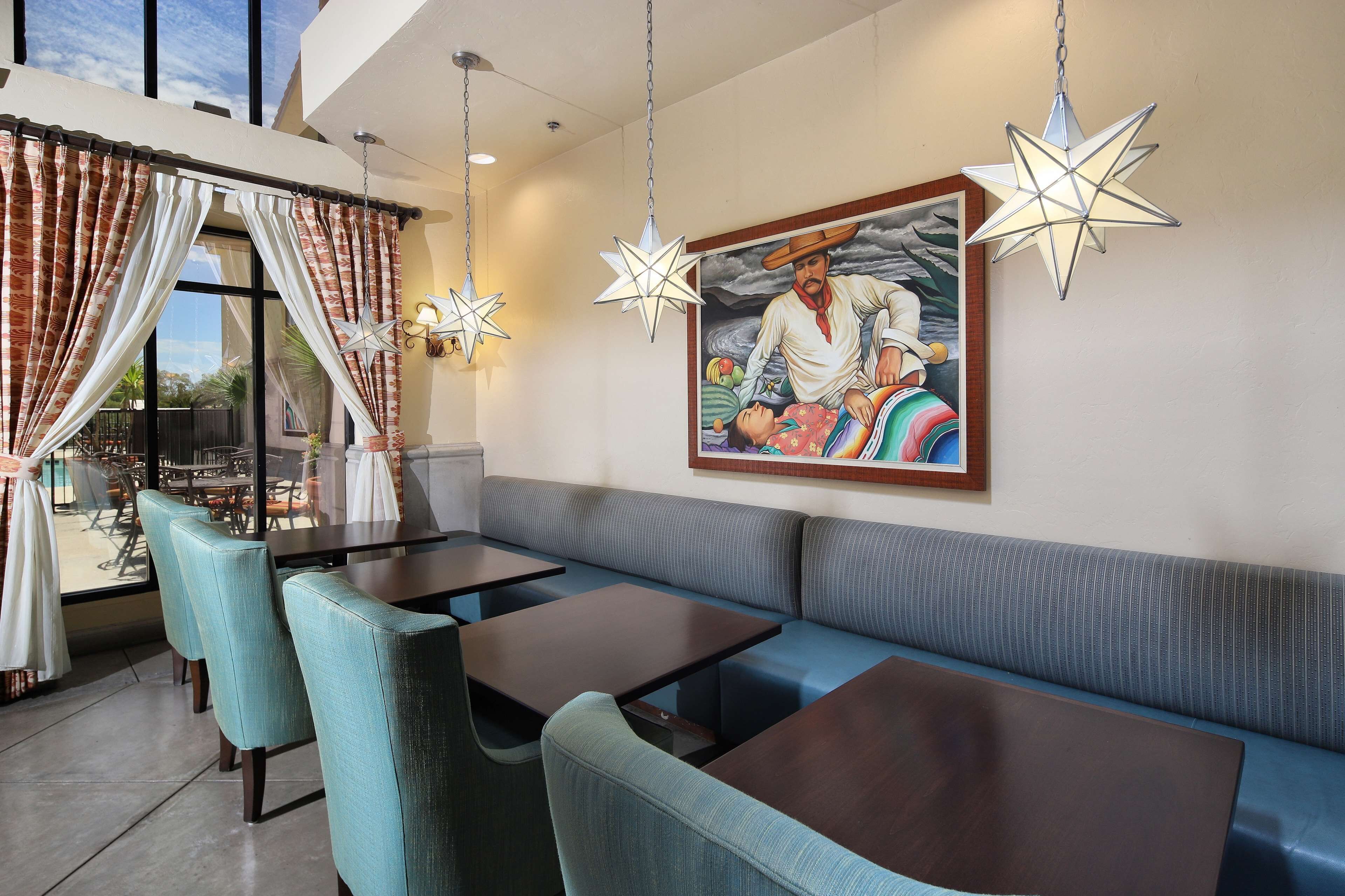 A restaurant with a high ceiling, star-shaped hanging lights, a large painting on the wall, and a view of the outdoors through large windows.