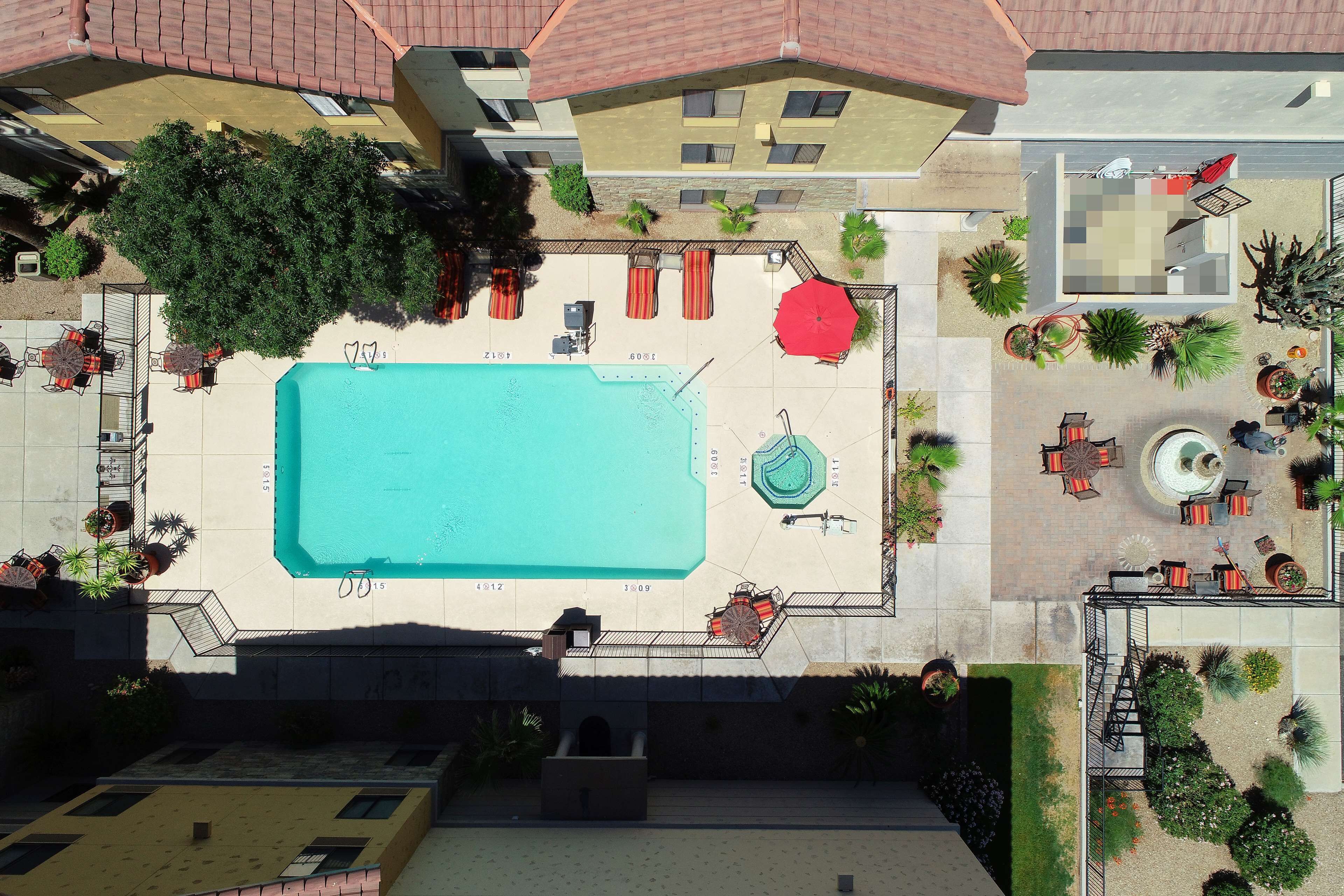 An aerial view of a hotel courtyard with a swimming pool, outdoor seating, and various plants.