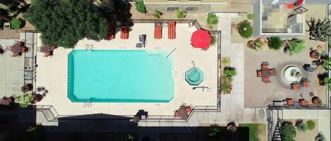 An aerial view of a hotel courtyard with a swimming pool, outdoor seating, and various plants.