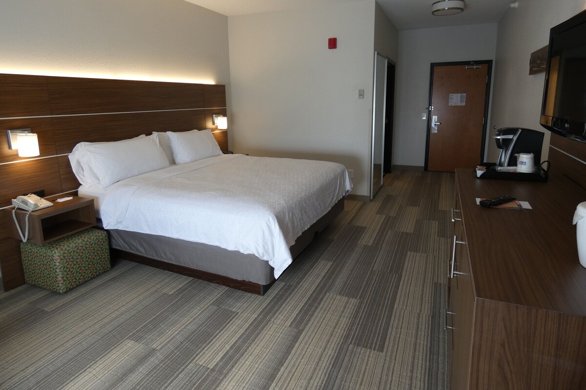 A hotel room with a bed, bedside table, lamp, and a TV.