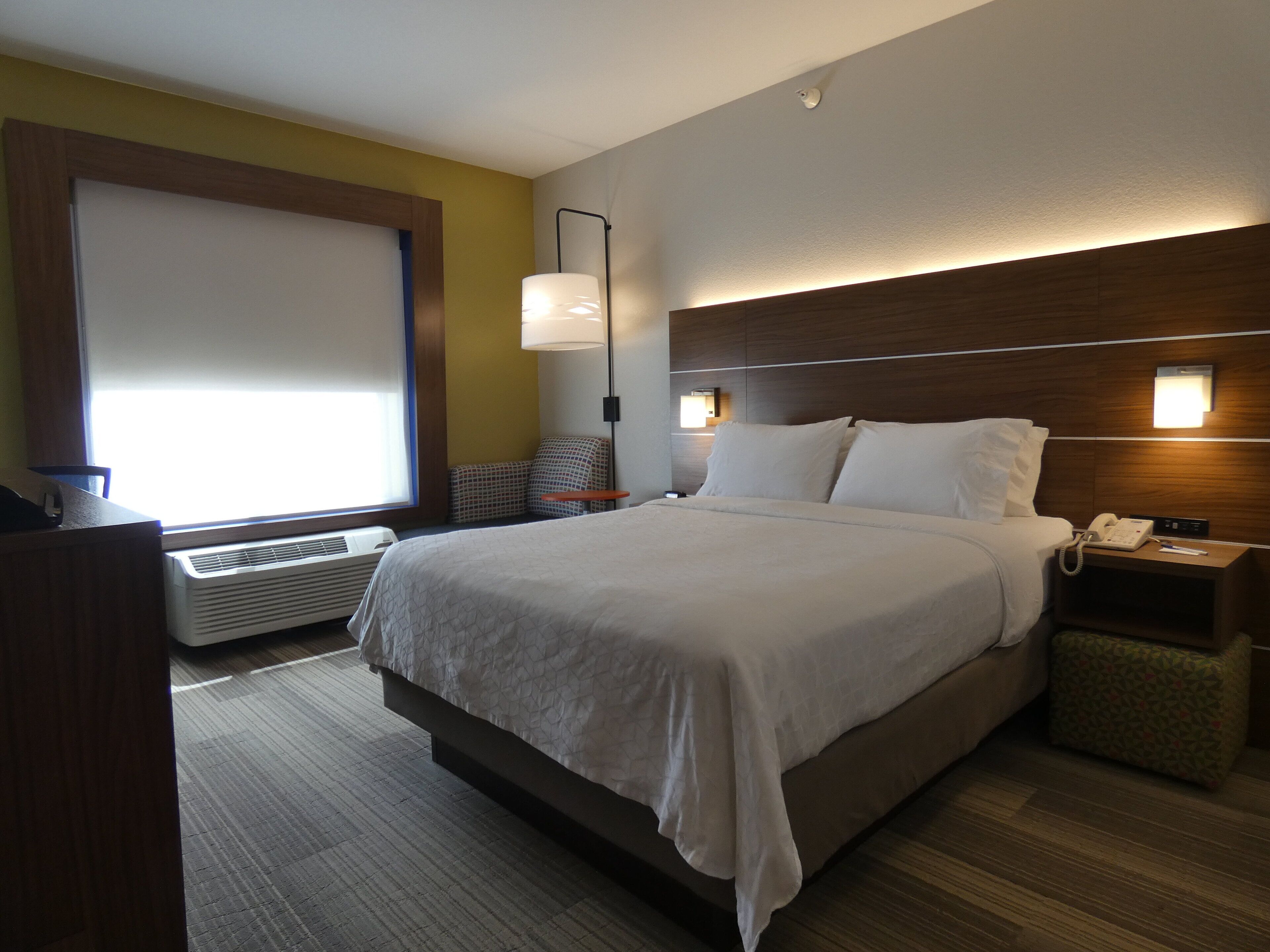 Una habitación de hotel con cama, mesita de noche, lámpara y ventana con persianas.