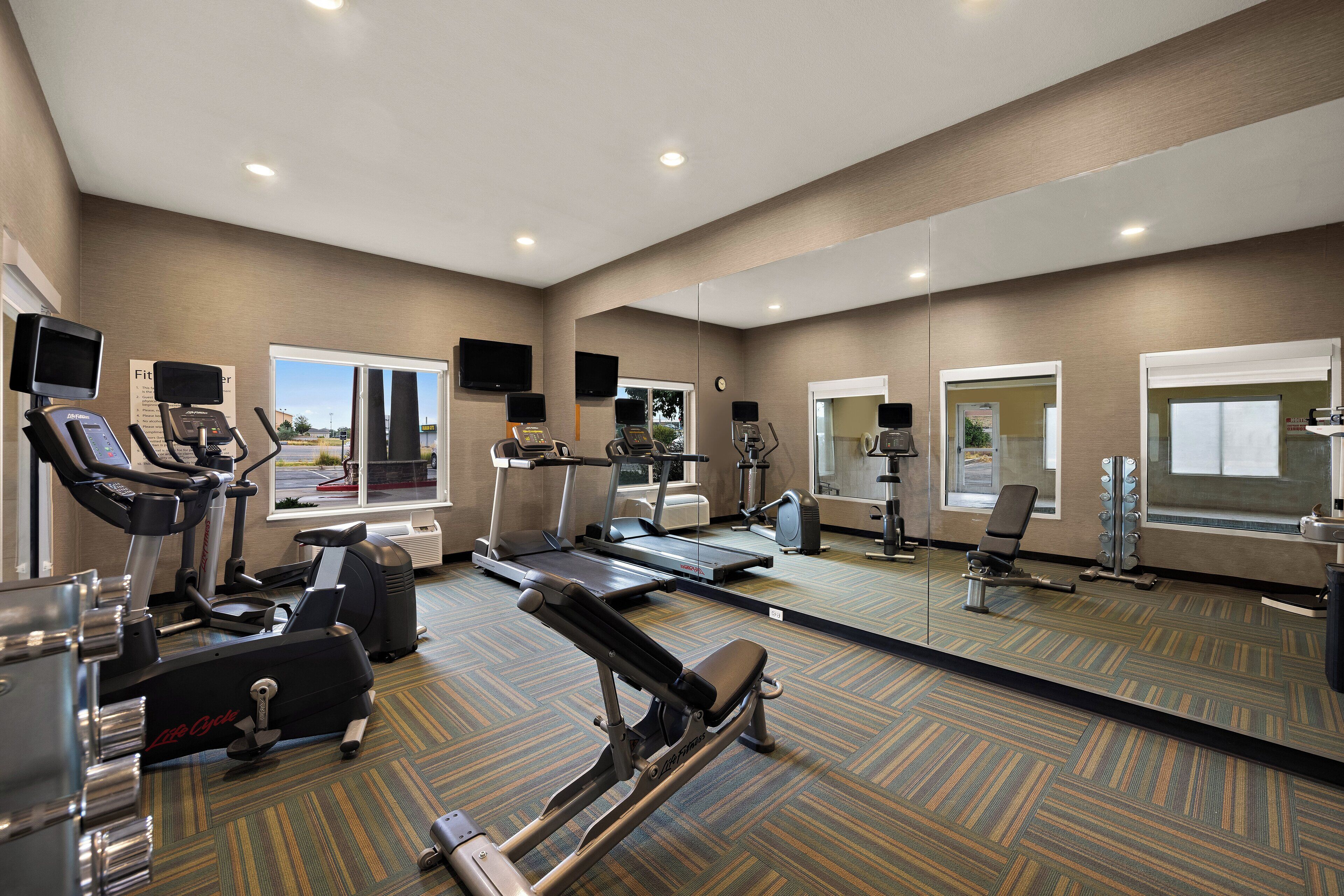 Un gimnasio con máquinas de cardio, equipo de pesas y un espejo grande.