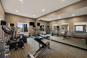 Un gimnasio con máquinas de cardio, equipo de pesas y un espejo grande.