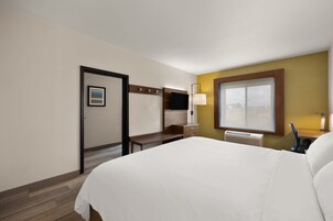 Una habitación de hotel con una cama grande, un escritorio con televisor de pantalla plana, una ventana con persianas y una puerta con un cartel.