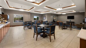 A spacious dining area with multiple tables and chairs, a kitchen area with wooden cabinets, and a large window providing a view of the outdoors. - Holiday Inn Express Hotel & Suites Limon I-70 by IHG (Limon)