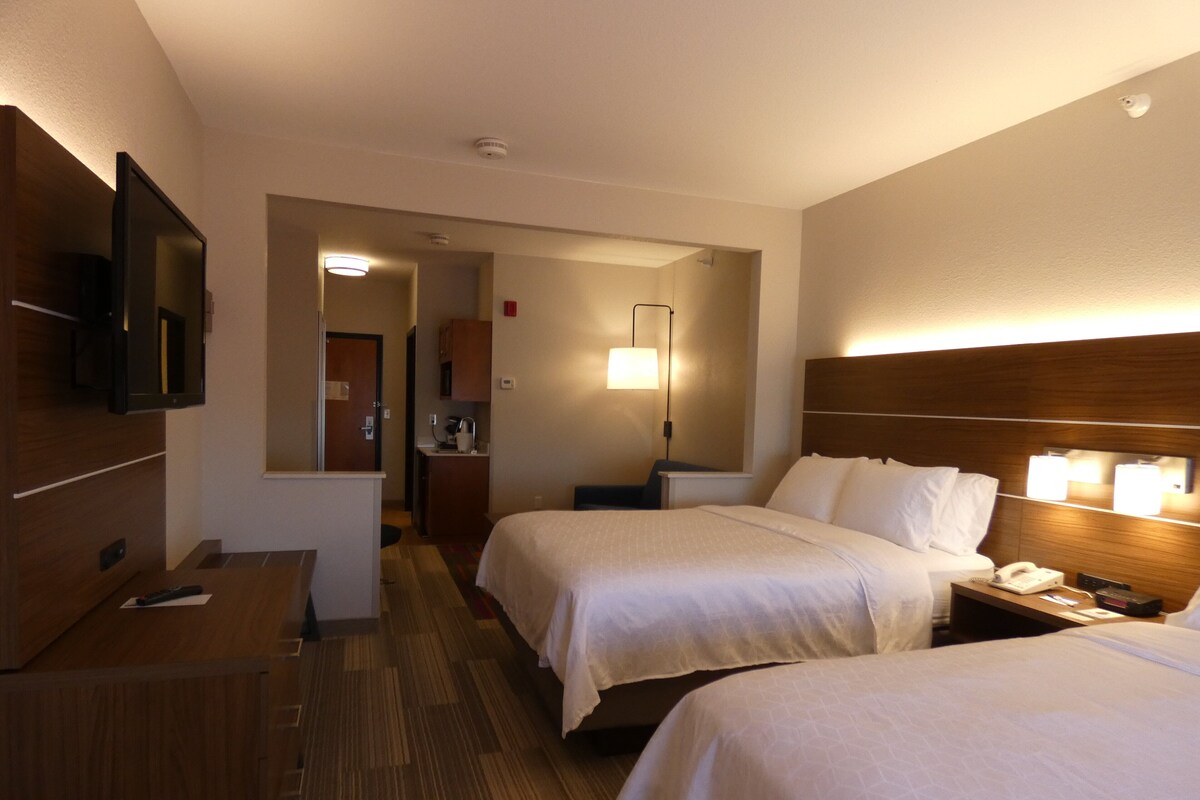 A hotel room with two beds, a TV, a desk, a lamp, and a bathroom visible through an open door.