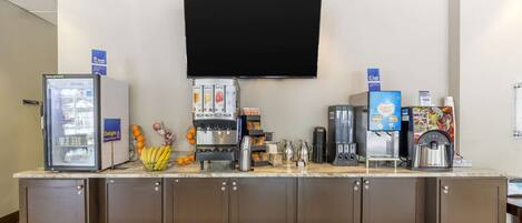 Un angolo colazione self-service con un frigorifero, macchine da caffè e un televisore a schermo piatto montato a parete.