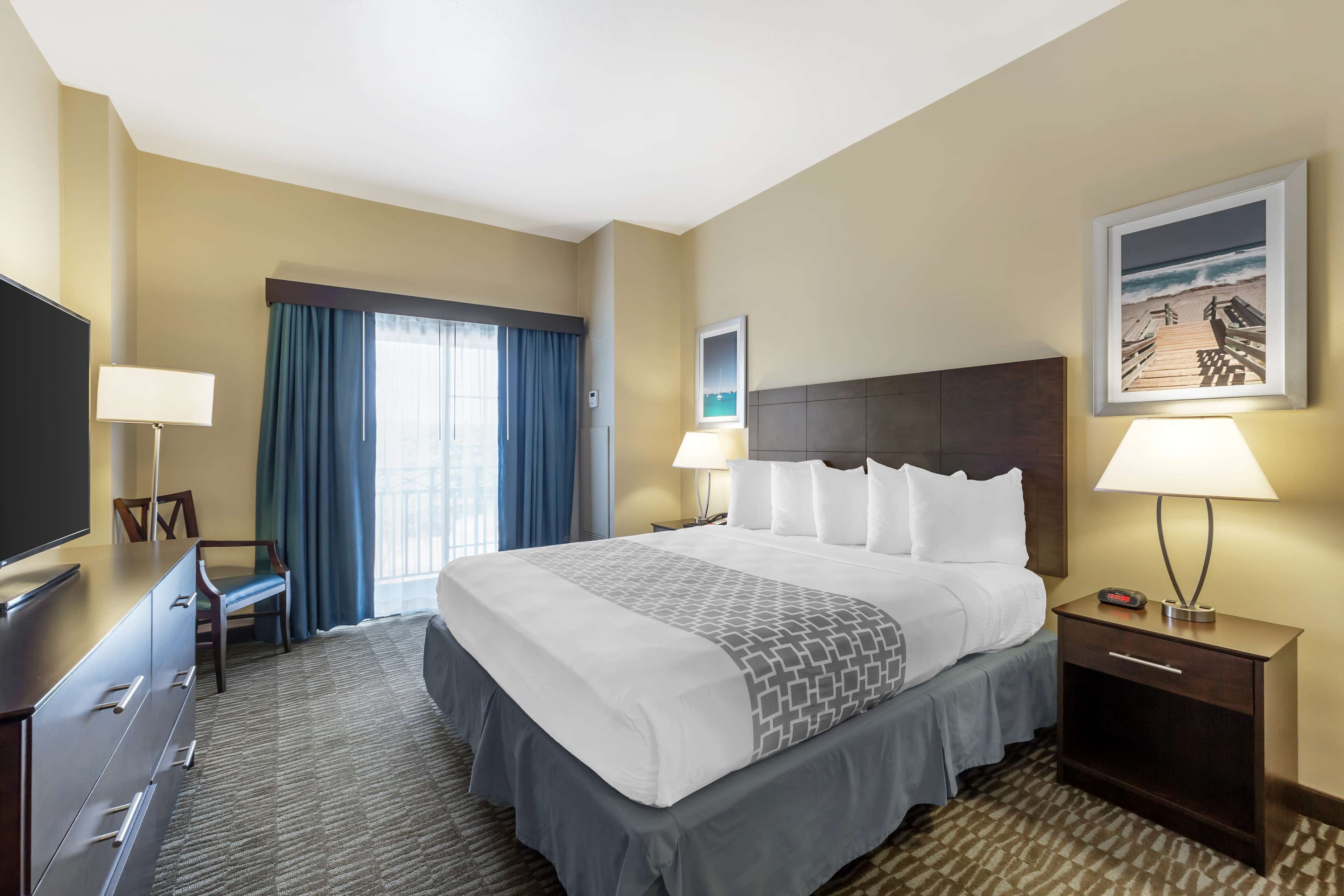 A hotel room with a large bed, a desk with a chair, a TV, and a nightstand with a lamp.