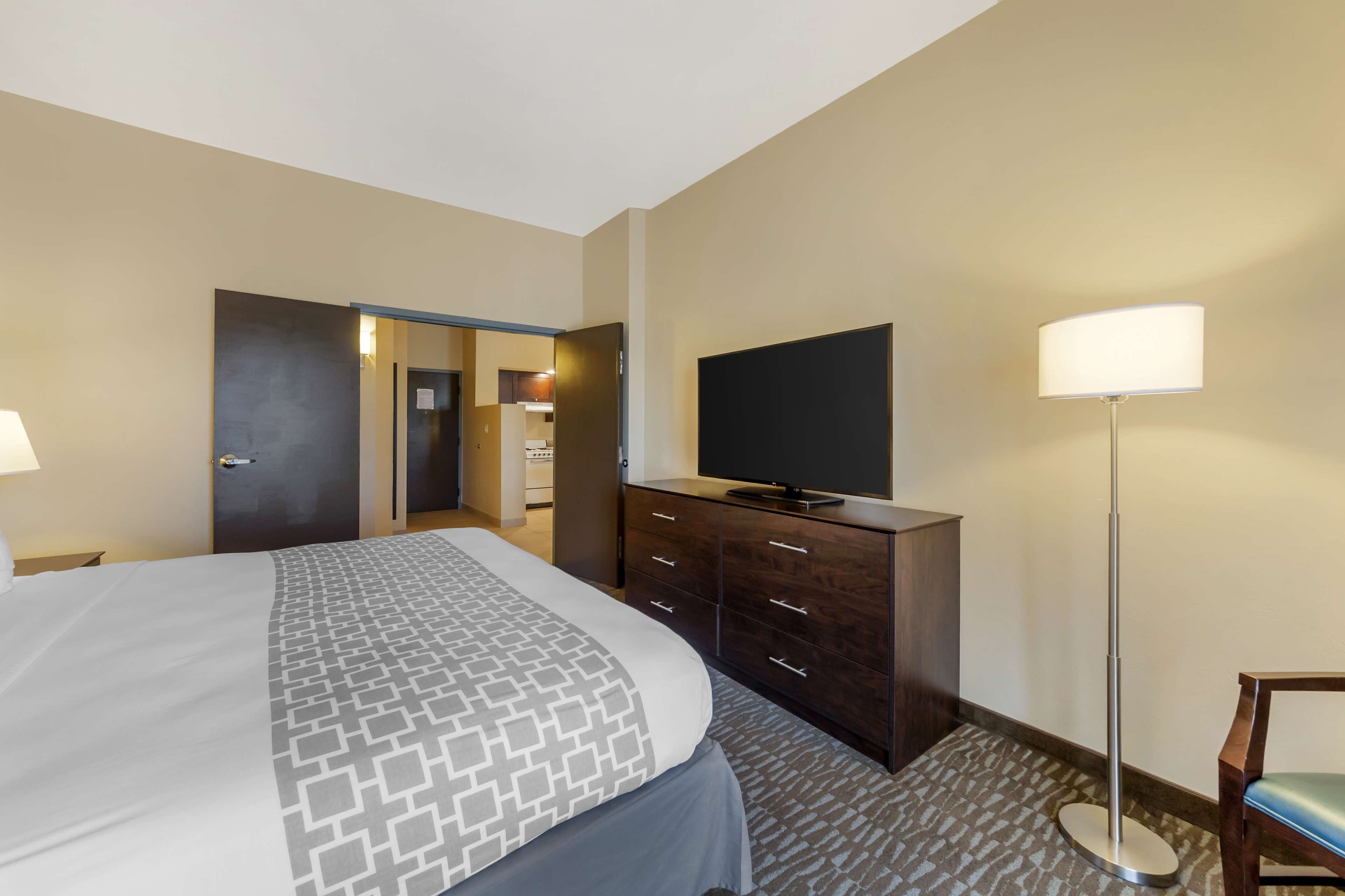 A hotel room with a large bed, a dresser, a television, and a floor lamp.