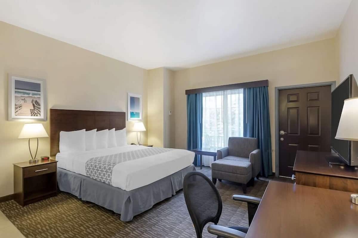 Une chambre d’hôtel comprenant un lit, deux lampes de chevet, une chaise, un bureau, une télévision et une fenêtre avec des rideaux.