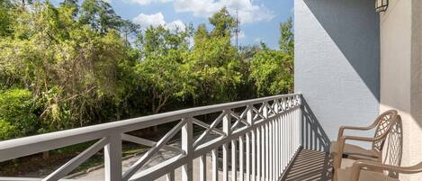 A balcony with a white railing overlooking a road and dense greenery.