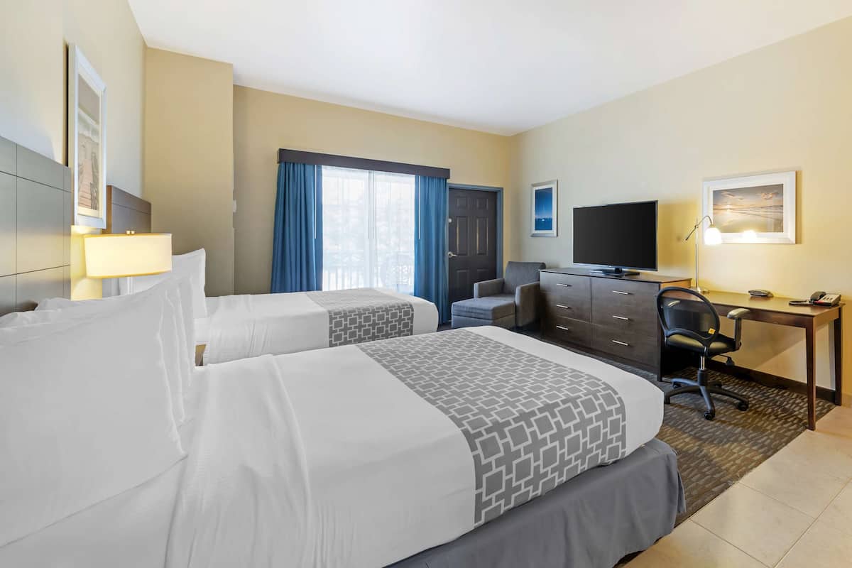 Une chambre d’hôtel avec deux lits, un bureau, une chaise, une télévision et une fenêtre avec des rideaux.