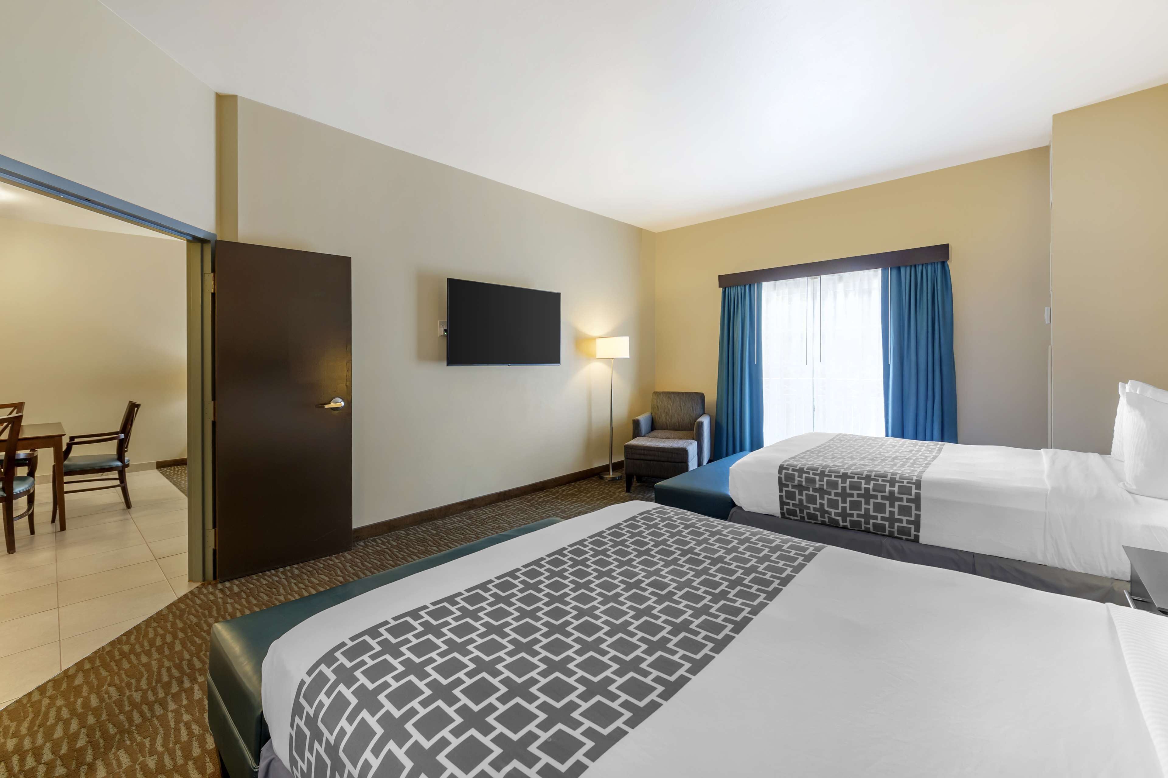 A hotel room with two beds, a desk, a chair, a flat-screen TV, and a window with curtains.