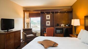 A hotel room with a bed, a TV, a desk, a chair, a lamp, and a microwave.