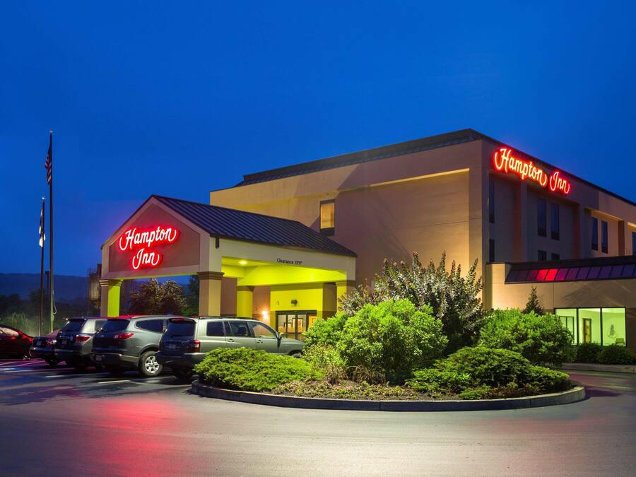 Un hotel Hampton Inn con un letrero de neón, un estacionamiento con varios coches y una zona verde bien cuidada al frente.