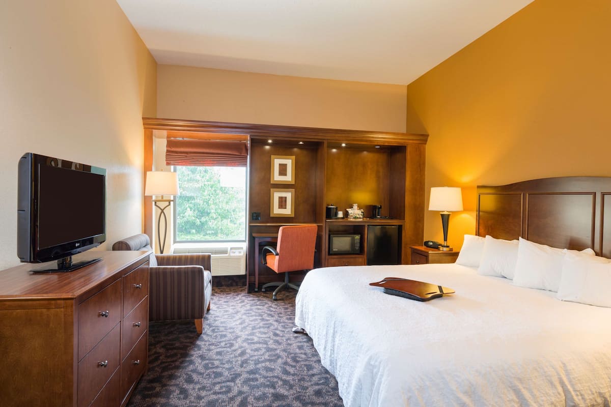 A hotel room with a bed, a desk, a television, and a window with blinds.