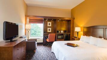 A hotel room with a bed, a desk, a television, and a window with blinds.