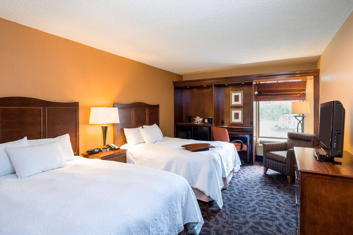 A hotel room with two beds, a desk, a chair, a television, and a window with blinds.