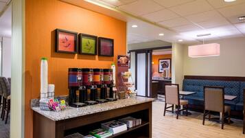 A hotel lobby with a coffee station, seating area, and framed artwork on the wall.