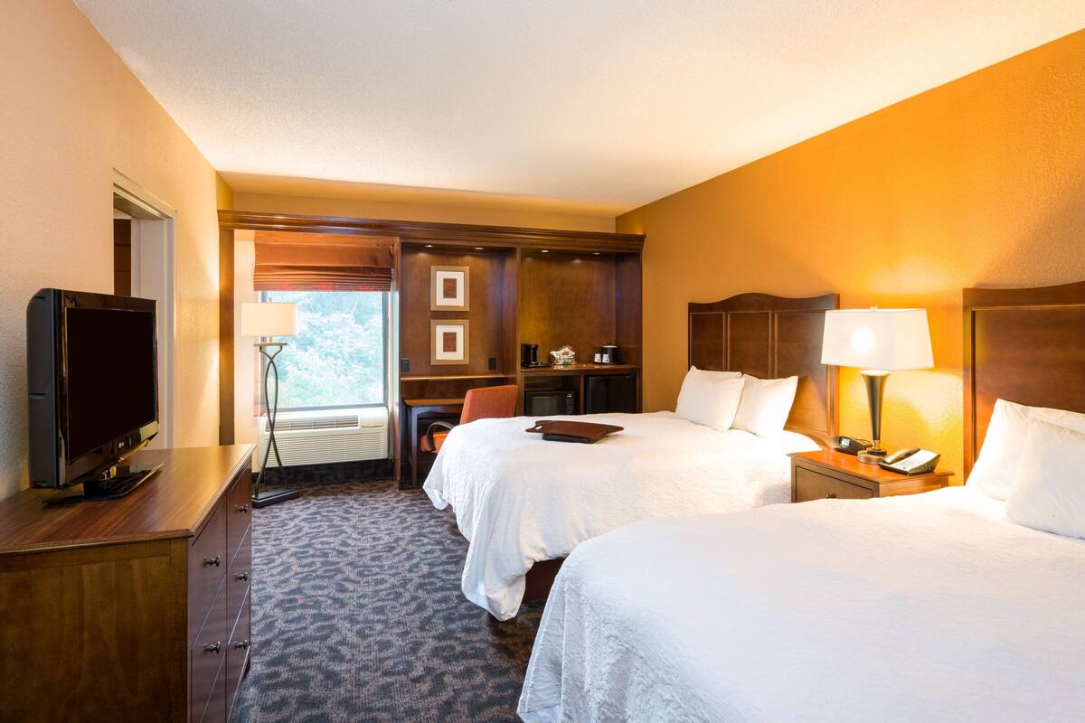 A hotel room with two beds, a TV, a desk, and a chair.