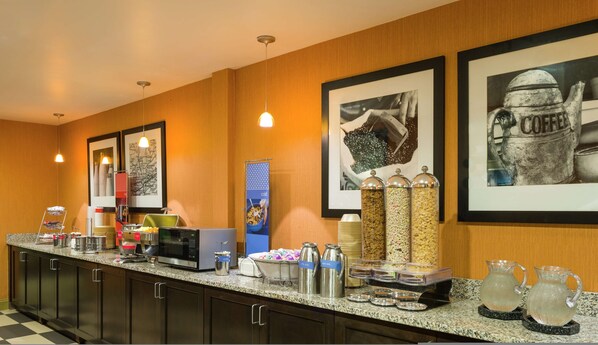 A hotel breakfast bar with various food items, a microwave, and a coffee station.