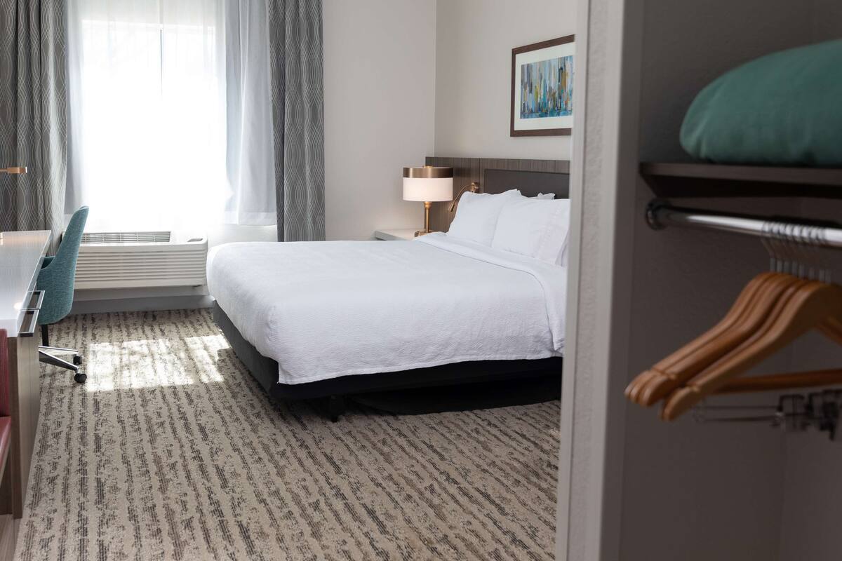 Habitación de hotel con cama, escritorio, silla, lámpara y un cuadro en la pared.