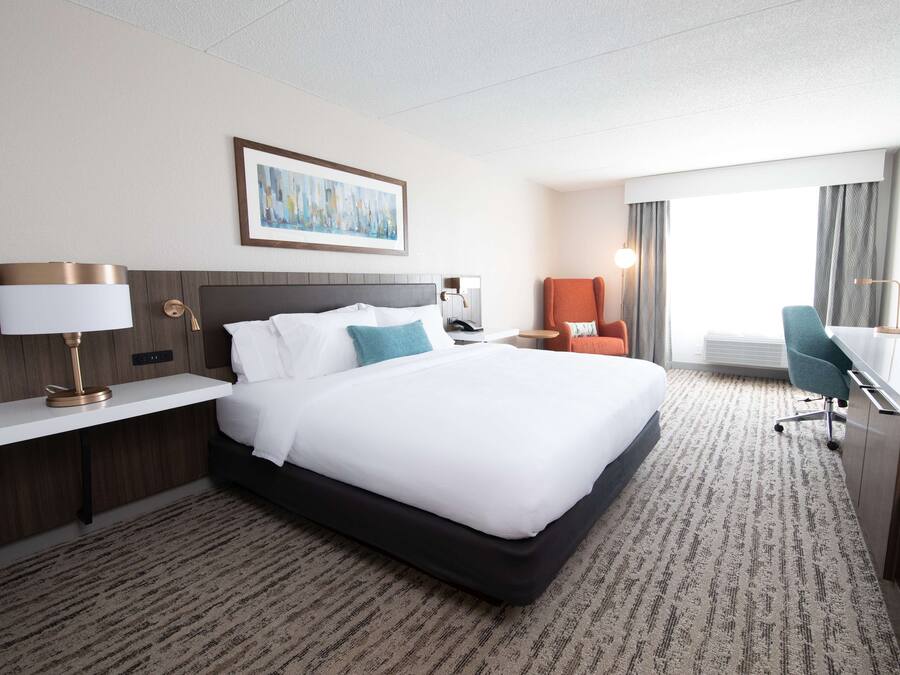 A hotel room with a large bed, a desk, a chair, and a painting on the wall.