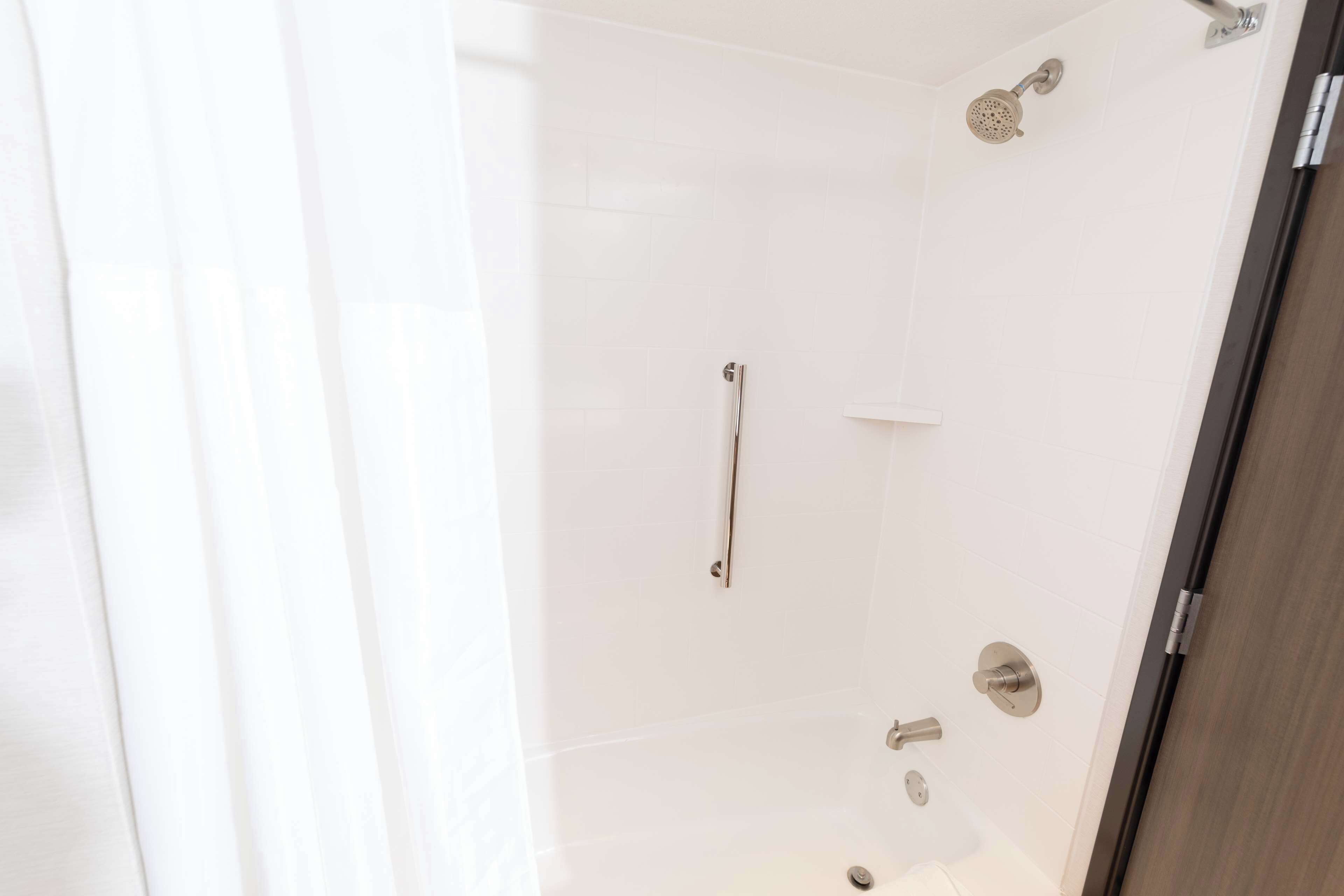 A modern shower with a handheld showerhead, a wall-mounted faucet, and a control panel.