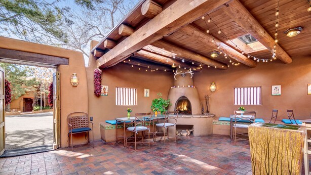An outdoor patio with a rustic wooden ceiling, a brick floor, and a stone fireplace. - Santa Fe Motel & Inn (Santa Fe)