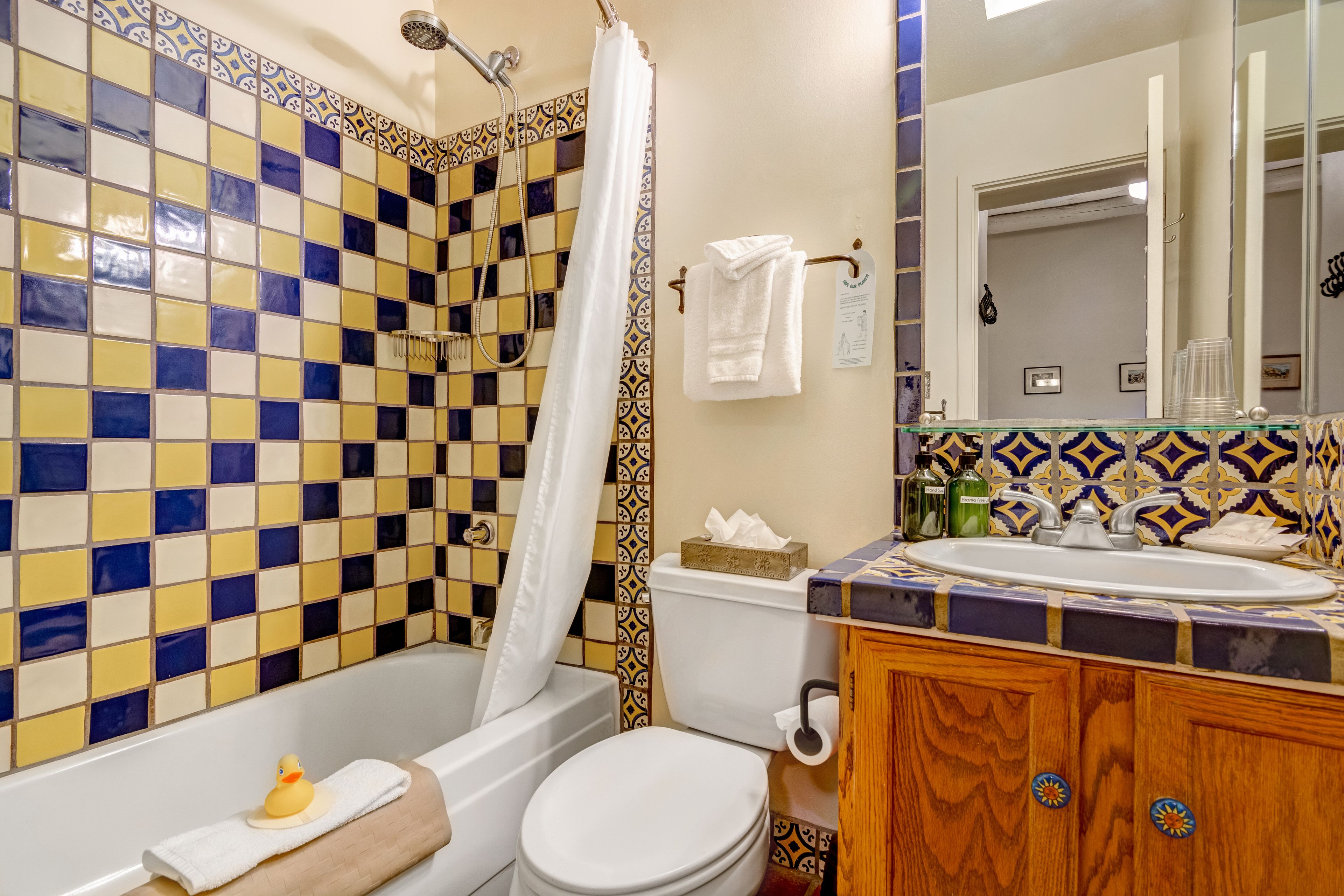 A bathroom with a checkered tile wall, a bathtub, a toilet, and a vanity with a sink and mirror.