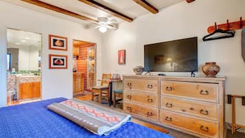 A bedroom with a bed, wooden dresser, television, and a bathroom visible through an open door.