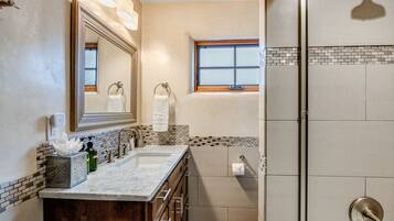 A bathroom with a double sink, a large mirror, a window, and a walk-in shower.