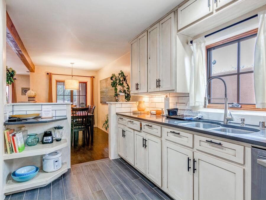 A modern kitchen with white cabinets, a double sink, and a dining area with a table and chairs.