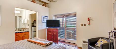 Quarto com cama, televisão, armário de madeira, cadeira e janela com persianas.