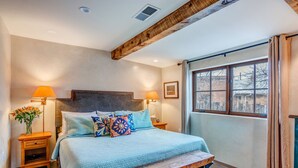 A bedroom with a large bed, two bedside tables, a bench, and a window with curtains. - Santa Fe Motel & Inn (Santa Fe)