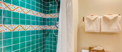 Un baño con paredes de azulejos verdes, una ducha, un inodoro y dos toallas colgadas en un perchero.