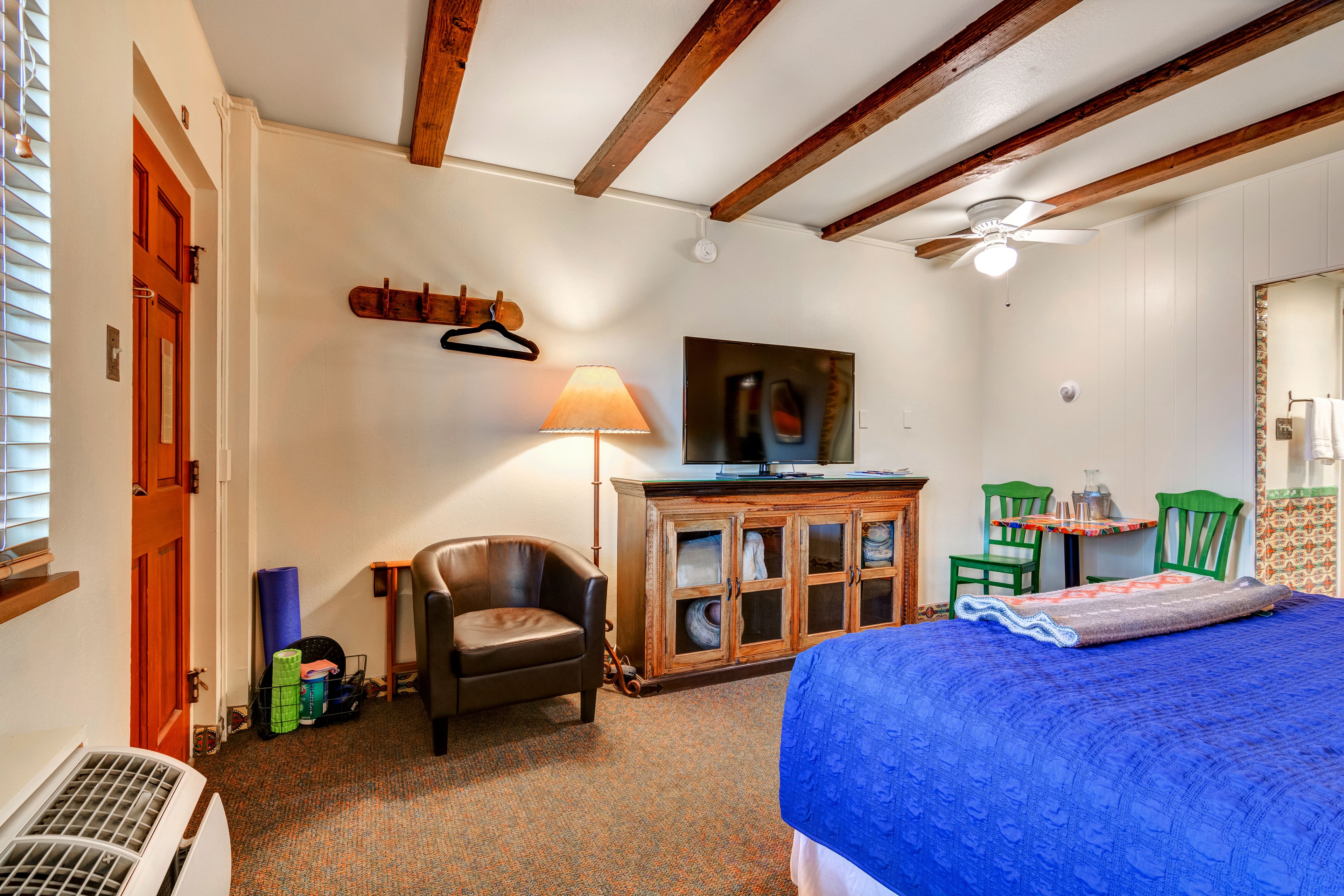 A bedroom with a bed, a chair, a desk, a lamp, and a television.