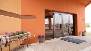 A building entrance with a wooden bench, potted plants, and a doormat. - Cities Of Gold Casino (Santa Fe)