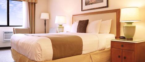 A hotel room with a large bed, two bedside tables with lamps, a framed picture on the wall, and a window with curtains.