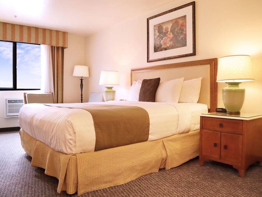 A hotel room with a large bed, two bedside tables with lamps, a framed picture on the wall, and a window with curtains.