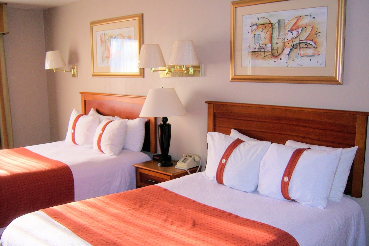 A hotel room with two beds, each with a red and white bedspread, a wooden headboard, and a nightstand with a lamp and a telephone.