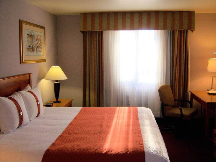 A hotel room with a large bed, a desk, a chair, a lamp, and a window with curtains.