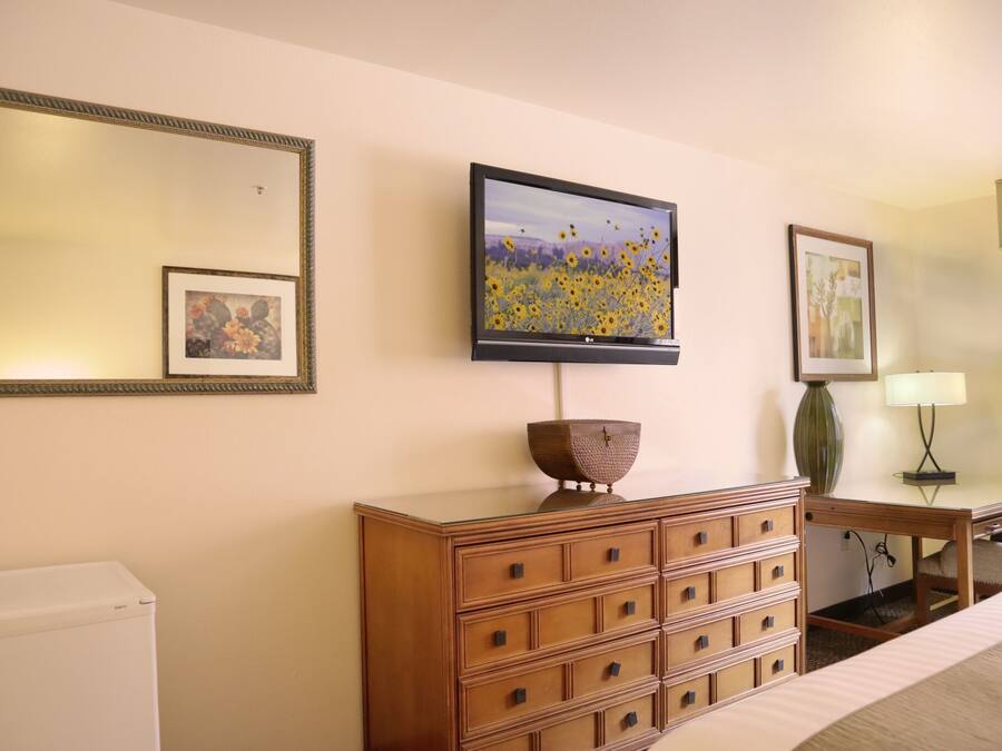 Une chambre d’hôtel avec une commode en bois, un téléviseur à écran plat fixé au mur, un tableau encadré au-dessus de la commode et une lampe sur une table d’appoint.